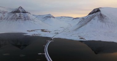 Sakin bir gölü geçen, sakin sularına mükemmel yansıyan karlı dağlarla büyüleyici bir hava manzarası.