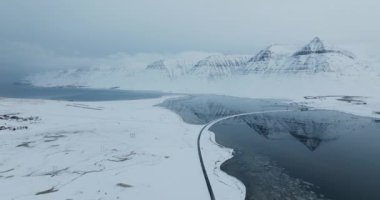 Karlı dağlar sakin bir göle mükemmel bir şekilde yansıyor, kışın dinginliğinin dingin güzelliğini yakalıyor.