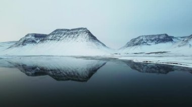 Karlı dağlar gölün durgun, camsı yüzeyine mükemmel bir şekilde yansıyor. Kış manzarasının dingin güzelliğini ve huzurunu gözler önüne seriyor.