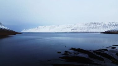 Uçsuz bucaksız bir kış manzarası, karla kaplı dağlar ve dingin bir göl, el değmemiş, karlı bir ortamın huzur veren güzelliğini yakalıyor.