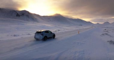 Akşam karanlığında karlı bir yolda yol alan bir arabanın hava görüntüsü.