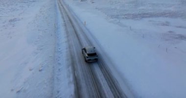 Karlı bir arazide giden bir arabanın kuş bakışı görüntüsü aracın uçsuz bucaksız kış manzarasında yaptığı yolculuğu yakalıyor.
