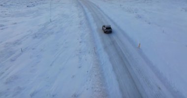 Karla kaplı bir yolda giden tek bir arabanın hava görüntüsü aracın kış manzarasında yaptığı yolculuğu gösteriyor.