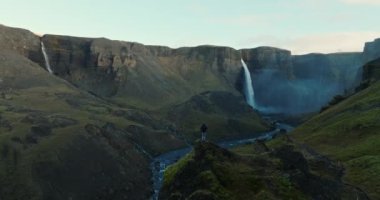 Bir hava yayı, kayalık bir çıkıntıda durup İzlanda 'daki görkemli Haifoss şelalesine bakarak doğal manzaranın ihtişamını vurgulayan bir adamı yakalar.