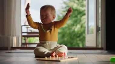 Bir bebek ahşap bir zeminde oturur, silindirik mandallarla ve ilgili deliklerle dolu tahta bir oyuncakla oynar. Doğal ışık büyük cam bir kapıdan geçer, yere gölgeler bırakır.