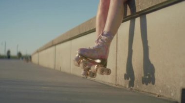 Alçak beton bir duvarın kenarından sarkan tekerlekleri olan renkli patenlerin yakın plan çekimi. Patenli kadın oturuyor.