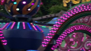 Yanıp sönen parlak mavi ve kırmızı ışıkların olduğu bir panayır gezisi canlı bir atmosfer yaratır. Dekoratif paneller arka planda görünür