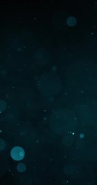 Yüzen parçacıkların olduğu karanlık bir arkaplan. Parçacıkların çoğu küçük ve odak dışı. Bokeh etkisi yaratıyor. Öncelikle maviler, ancak bazılarında yeşil ve turkuaz ipuçları var.