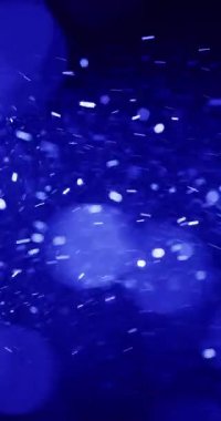 Sayısız küçük, beyaz parçacıklar koyu mavi bir arkaplan boyunca hızla hareket ediyorlar. Bu parçacıkların boyutları ve şekilleri farklıdır, bazıları uzun çizgiler, bazıları ise küçük noktalar olarak görünür.