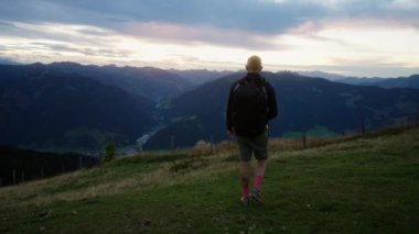 Arkadan bakıldığında, bir adam yürüyor ve Avusturya 'nın nefes kesen dağlarına bakıyor. Önünde büyüleyici bir dağ manzarası var.