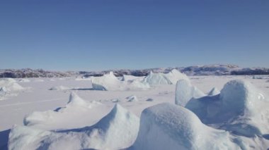 Grönland 'ın çarpıcı buz oluşumlarının ve karlı dağlarının hava manzarası berrak mavi bir gökyüzüne doğru ilerliyor.
