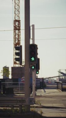 Bir direğin üzerindeki yaya trafik ışığı yeşil yürüyen bir figür gösterirken, yayaların geçmesinin güvenli olduğunun sinyalini veriyor, arka planda ise bir yaya, bir inşaat vinci yer alıyor.