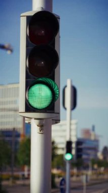 Yakın çekim bir direğe takılmış bir trafik ışığı içerir. Işık yeşilden kırmızıya geçer. Arka plan, bulanık bina hatlarıyla şehir mimarisine ait bir ipucunu gösteriyor.