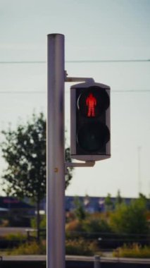 Yakından çekilen bir fotoğrafta kırmızı-yeşile dönüşen yaya trafik ışığı görülüyor, açık bir gökyüzü, ağaçlar ve yakındaki iyi aydınlatılmış bir yol ile yürüyen bir insan sembolü sergileniyor.