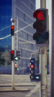 Şehir merkezindeki bir seri trafik ışıkları kırmızı ve yeşil sinyallerin karışımını gösteriyor. Bu da modern bir bina ve arka planda geçen arabaların durduğunu ve araçlara doğru gittiğini gösteriyor.