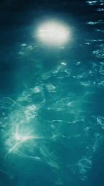 Güneş ışığı suyun üzerinde dans ederken parıldayan bir havuz yüzeyinin yakın çekim görüntüsü büyüleyici bir yansıma gösterisi yaratıyor.