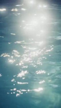 Parlak güneş yansımalarıyla parıldayan mavi bir havuzun yakın görüntüsü.