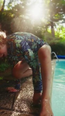 Küçük bir çocuk havuzdan çıkar ve tahta bir sopa kapar, onu dikkatlice su yüzeyinde yüzen bir yaprağı almak için kullanır.