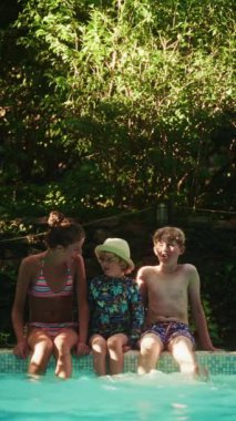 Çocuklar havuz kenarında oturur, suya tekme atar ve neşe saçar, kahkahaları ve heyecanları sahneye canlılık katar.