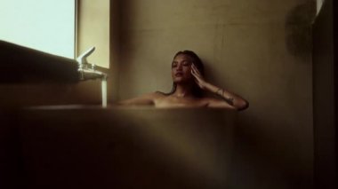 Bir kadın küvette dinlenir ve kendini şımartır, musluktan akan suyun rahatlatıcı zevkini çıkarırken sakin bir ortamda dinlenir.