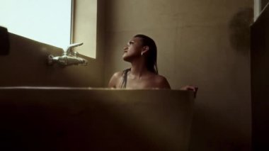 Rahat bir kadın küvette sırılsıklam, pencereden dışarı bakıyor ve huzur dolu bir yalnızlık ve sükunetin tadını çıkarıyor.