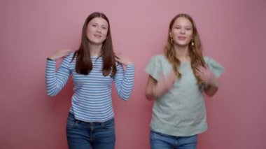 İki kız her hareketinde neşe ve enerji saçan canlı pembe bir arka plana karşı neşeli bir dans gösterisi sergiliyor.