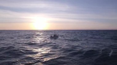 Sakin bir okyanusun üzerinde sakin bir gün doğumu, ufka doğru zarif bir şekilde ilerleyen küçük bir tekne.