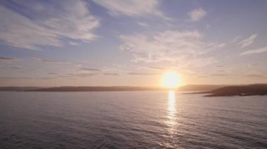 Günbatımında Norveç adalarını çevreleyen parlak suların üzerinde soldan sağa doğru kayan çarpıcı bir dron atışı sorunsuzca süzülür.