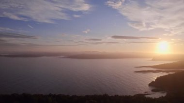 İnsansız hava aracı görüntüleri, siluetli Norveç adalarını ve ışıldayan denizleri büyüleyici bir şekilde yakalıyor. Gün batımı sakin suların üzerine altın rengi döküyor ve parlak bir yansıma yaratıyor.