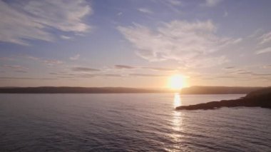 Günbatımında parlayan Norveç denizleri ve siluetli adaların çarpıcı manzarası, batan güneşin sakin suların üzerine sıcak, altın bir parıltı saçması ve büyüleyici bir yansıma yaratması.