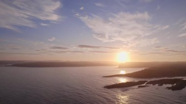 Günbatımına karşı gölgelendirilmiş Norveç adalarının sakin güzelliklerini, akşam gökyüzünün sıcak, altın renklerini yansıtan parıldayan sularıyla geri çekiliyor.