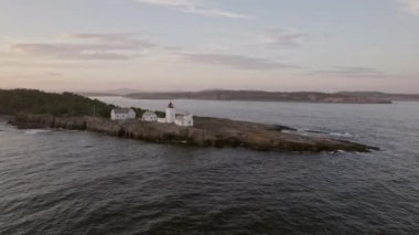 Drone ark, engebeli kayalık kıyılara tünemiş Langoytangen Deniz fenerini yakalıyor. Arka plandaki adaların geniş bir manzarası var.