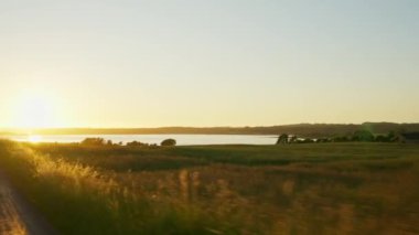 Canlı bir günbatımı gökyüzünün altında çimenli bir tarladan geçerken zengin renkleri ve manzaranın huzurlu güzelliğini yakalıyorum.