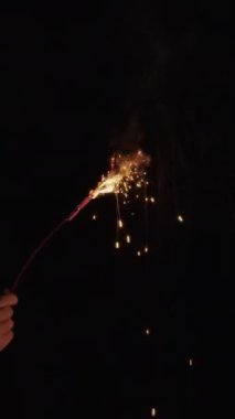 Elinde yanan bir maytap karanlık bir gece gökyüzüne karşı parıldıyor, neşeli ve büyüleyici bir ışık gösterisi yaratıyor
