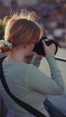 Çatı katındaki kız fotoğrafçı şehir manzarasını yakalıyor. Sıcak gün batımı ışığı onu altın saat boyunca aydınlatıyor. Mükemmel bir kare oluşturuyor.
