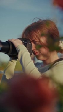 Altın saat boyunca ön planda bulanık bitkilerle çekim yapan bir kadın fotoğrafçı, sıcak ve yumuşak ışığı yakalıyor.
