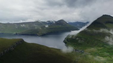 Puslu bulutlar, Faroe Adaları 'ndaki engebeli yeşil tepeleri ve çevresindeki suları kaplayarak dramatik ve ruhani bir manzara yaratır.