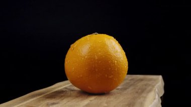 Işık altında parıldayan su damlacıkları ile parlak, ıslak bir portakal, karanlık bir zemin üzerine kurulmuş.