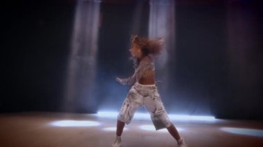 Zarif bir şekilde hareket eden bir kadının büyüleyici bir sahnesi, parlak beyaz ışıklı ışıklarla kaplanmış, akışkan hareketlerini karanlık bir zemine vurguluyor.