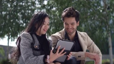 İki meslektaş dışarıda, tablete bakarken bir sohbete dalıyorlar. Kadın adama bir şey anlatıyor, adam gülümsüyor ve etkileşimden hoşlanıyor gibi görünüyor.