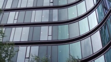 Düşük açılı bir çekim, parlak cam cepheli modern bir ofis binasını yakalar, geniş dikdörtgen pencereler, dalgalı bir şekilde düzenlenir ve dinamik bir görsel etki yaratır.