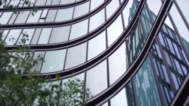 Yakın çekim, modern bir ofis binasının cam cephesinin kıvrımlı tasarımını, dinamik görsel akış yaratan eğri büğrü bir şekilde sıralanmış büyük yansıtıcı pencereleriyle vurgular.