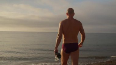 Güneş doğarken yüzmek için denize doğru yol alır, yumuşak sabah ışığı suyu aydınlatır ve plajda sıcak bir parıltı yayar.