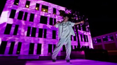Platformda bir hip hop dansı performansı, sahnenin enerji ve görsel etkisini artıran canlı pembe bir cephe karşısında yanıp sönen ışıklarla aydınlatılır.