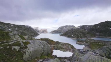 Engebeli yaban ve kayalık arazilerle çevrili sakin bir Norveç gölü, dingin sularla sert, doğal manzara arasındaki zıtlığı vurguluyor.