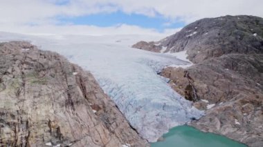 Engebeli, kayalık bir arazide, uzak ve el değmemiş bir arazide buzla pürüzsüz arazi arasındaki çarpıcı zıtlığı vurgulayan Norveç buzulunun çarpıcı bir hava görüntüsü.