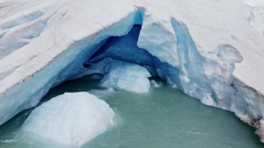 Nigardsbreen Buzulu 'nun iç kısımları pürüzsüz ve kıvrımlı olan sıkıştırılmış buzdan yapılmış mavi buz tünelinin ve yüzeyinden yükselen erimiş su akıntısının yakın çekim görüntüsü.