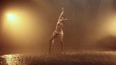 Arkasındaki parlak turuncu ışıkla aydınlatılan bir yağış altında zarif bir performans sergileyen bir kadın büyüleyici ve canlı bir görsel etki yaratır.