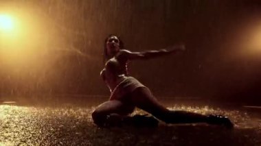 Büyüleyici bir performans, yağmurda duygularını ve yaratıcılığını ifade eden, arka planda parlak turuncu ışıklarla vurgulanan bir kadın dansçıyı yansıtıyor.