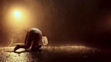 Cesur ve kendinden emin bir kadın cesur bir kıyafetle dans yeteneğini sergiliyor. Yağmurda canlı turuncu ışıkların önünde zarif bir performans sergiliyor.